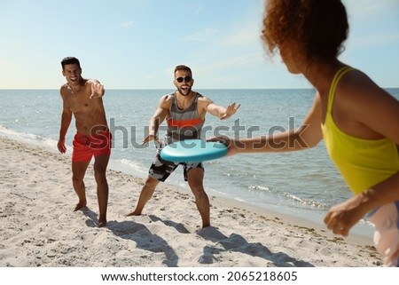 Friends playing with flying disk at beach on sunny day