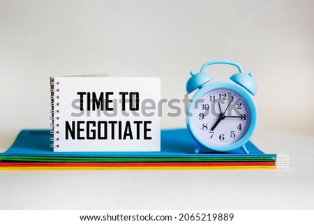 In a notebook, the text TIME TO NEGOTIATE next to multi-colored folders and a clock on a white
