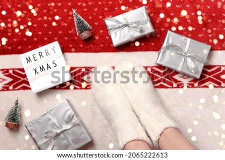 Close-up of female legs in warm socks with christmas gifts, miniature christmas trees and lightbox with text merry xmas.