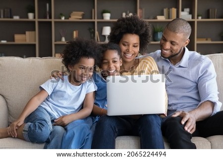 Happy loving african american family couple parents and little cute children son daughter using computer, enjoying shopping in internet store or watching funny cartoons online, resting on sofa at home