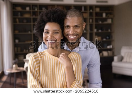 Portrait of happy loving young mixed race family couple posing in modern living room. Smiling bonding millennial homeowners celebrating moving into own apartment, good family relations concept. Royalty-Free Stock Photo #2065224518