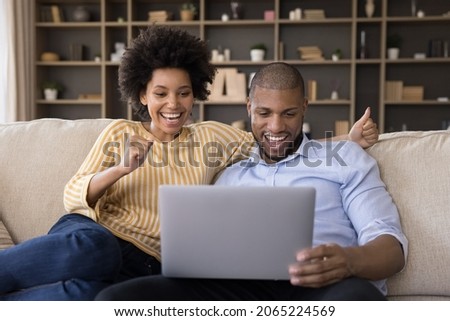 Joyful sincere laughing young african american family couple celebrating internet success, getting online lottery giveaway gambling auction win notification, feeling excited looking at laptop screen. Royalty-Free Stock Photo #2065224569
