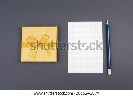Empty paper, a pen and a golden colored gift on a dark grey background, copy space for text
