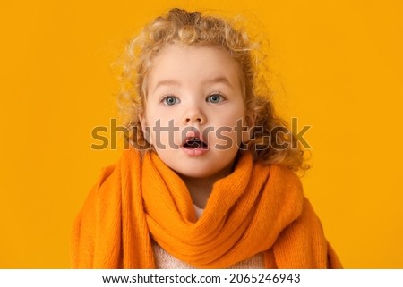 Cute little girl with warm scarf on color background