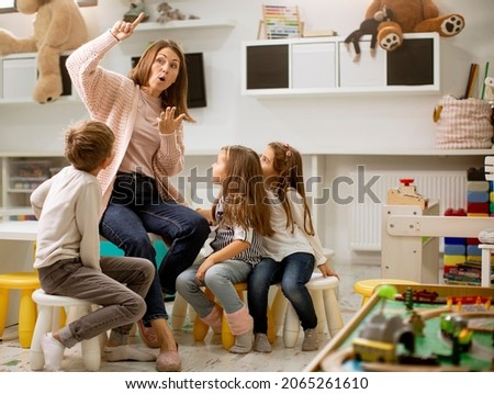 Nursery teacher talking story to group of children sitting on a small chairs at kindergarten Royalty-Free Stock Photo #2065261610