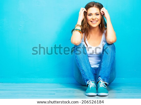 Hipster girl sitting on floor against blue background. Royalty-Free Stock Photo #206526184