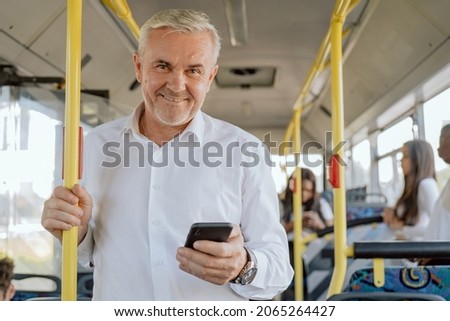 Older man with gray hair wearing shirt travels by bus with smile businessman goes to work retiree takes public transportation to go shopping church family holds phone in hand buy ticket through apps Royalty-Free Stock Photo #2065264427