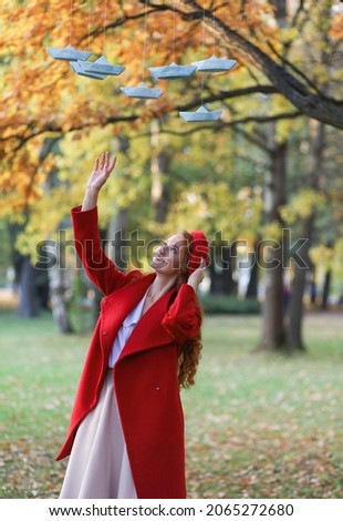 A girl with long red hair, in a red coat and beret walks in the park, in the fall. Photo sessions in nature, walk, decor