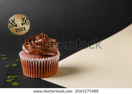 Tasty cupcake for New Year 2022 celebration on dark background
