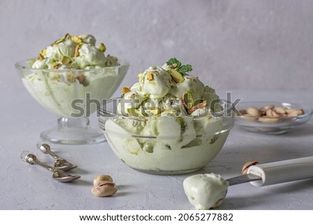 Pistachio ice cream with nuts in two transparent glass ice-cream bowl on a gray background.