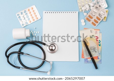 Cost of health care with EURO bank notes, stethoscope, notebook, medicaments. Price of medicine. Medical expenses. EURO small bills cash money. Cost of medicinal products, treatment concept. Top view