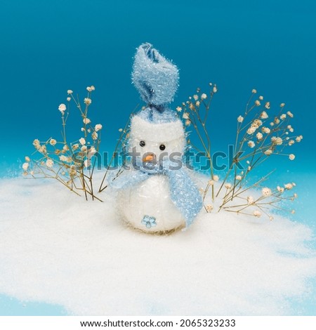 Snowman with a hat on his head and snow twigs behind him stands on the cold snow and has a flower on his stomach