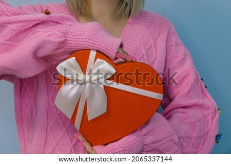 Girl holding a gift in a red box in the shape of a heart.Light background, selective focus.Concept - black friday, holiday, birthday, womens day