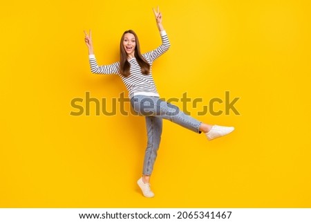 Full body photo of funny brunette millennial lady show v-sign wear jumper jeans sneakers isolated on yellow color background
