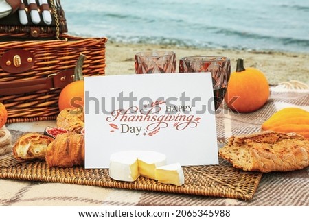 Glasses of wine, delicious food and card with text HAPPY THANKSGIVING DAY on beach, closeup