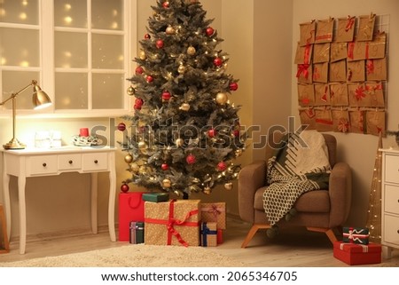Christmas tree, gift boxes, armchair and advent calendar on wall in room