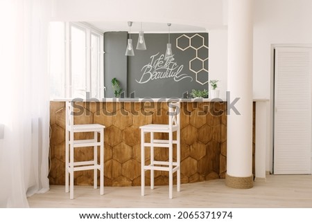 A stylish modern bar counter decorated with wooden tiles and two white bar stools in the living room of the house. Scandinavian interior design Royalty-Free Stock Photo #2065371974