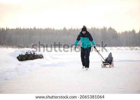 Young happy mother and little baby boy son sledding on snowy winter lake together