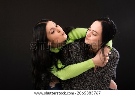 two attractive young womens having fun, one carries the other on her back and laughs, isolated on black