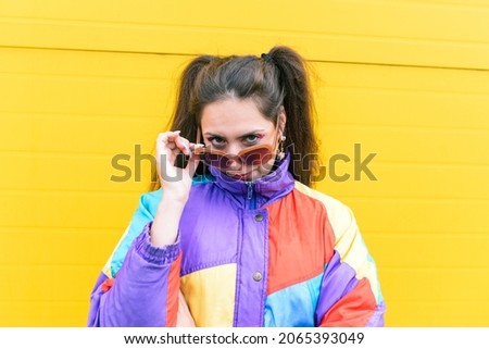 Fashionable girl in glasses and a colorful jacket near the yellow wall. Youth and street style concept.