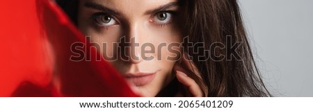 brunette young woman looking at camera near red glass isolated on grey, banner