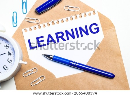 On a light background, a craft envelope, an alarm clock, paper clips, a blue pen and a sheet of paper with the text LEARNING
