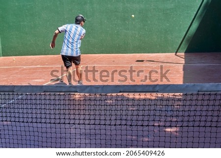 latin brunette man on his back playing paddle tennis alone, wearing a cap and an argentina t-shirt on vacation.horizontal