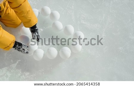 The child lays out heart-shaped snowballs on the ice. Icy snow background with copy space. Winter games on vacation. Making snowballs on a frosty day