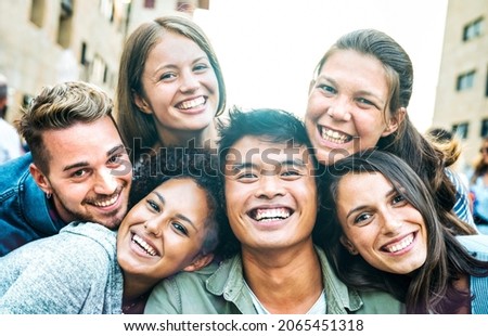 Multicultural men and women taking selfie out side with backlight - Happy milenial life style concept on young multiracial friends having fun day together - Bright azure filter with sunshine flare