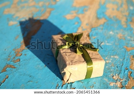 Wrapped vintage gift box with olive silk ribbon bow on blue (turquoise) old wooden background. Present box in craft paper with green bow with shadow. Holiday concept. Close-up. Side view.