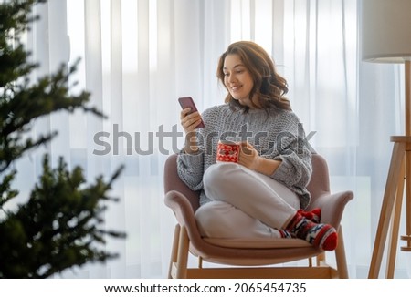 Woman is using mobile phone in the living room decorated for Christmas.