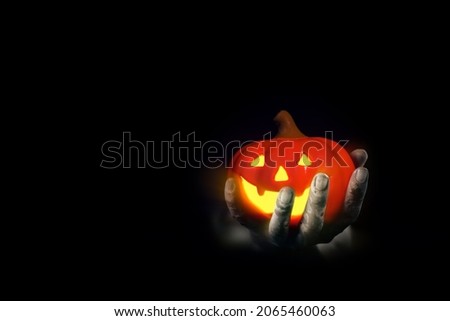 Spooky pumpkin that symbol of Jack o' Lantern glowing in scary pale hand hidden in black background. Horror photo for Halloween festival concept.