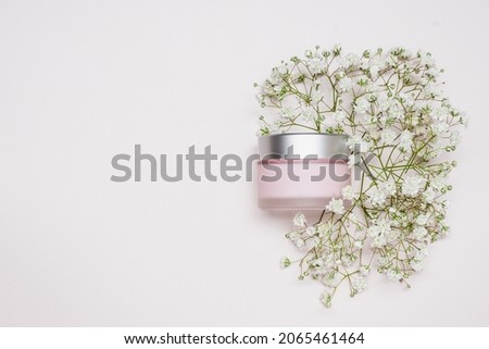 Jar of pink cosmetic face care cream. Beauty product on a pastel pink overflow among flowers