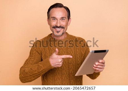 Photo of cool brunet man point tablet wear knitwear sweater isolated on beige color background