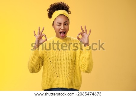 Okay I got it. Cute reliable truthful african-american girlfriend assuring friend secret safe winking devious hinting work done okay show ok fine perfect gesture no worry about, yellow background Royalty-Free Stock Photo #2065474673