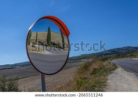 Cypress tree reflected in a convex traffic mirror. Tuscan landscape