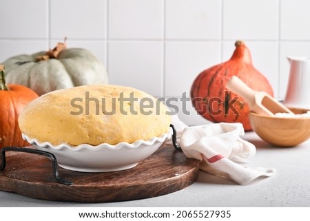 Raw yeast dough with pumpkin in white bowl covered with towel on the floured kitchen table, recipe idea. Concept home baking bread, buns or cinnabon or making dough.