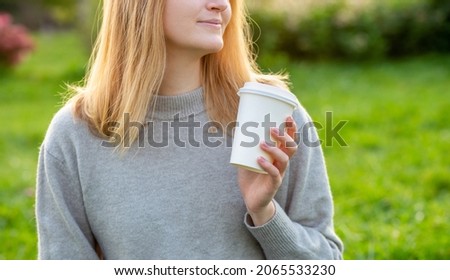Close up portrait of an attractive young blonde woman drinking coffee at summer park. Food, rest, Take away concept. Place logo on mug, mockup. Girl holding paper cup over nature background,