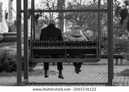 Black and white photo of an elderly man old man grandfather sitting together with his grandson on a swing in the city of MoscowGenerational Relationship Concept. 