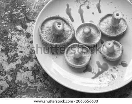Black and white photo of milk cap mushrooms on ceramic plate on rust iron background. Edible red pine mushroom pattern. Rich protein source food. Forest autumn harvesting. Natural texture.