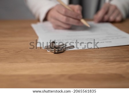 Property keys on desk with real estate contract and agents hands with pen and copy space on wood desk.