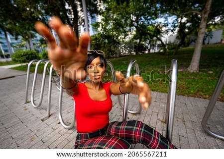 Photo of a beautiful female model posing outdoors in a park scene. Woman is posing by a metal bike rack in the park. 