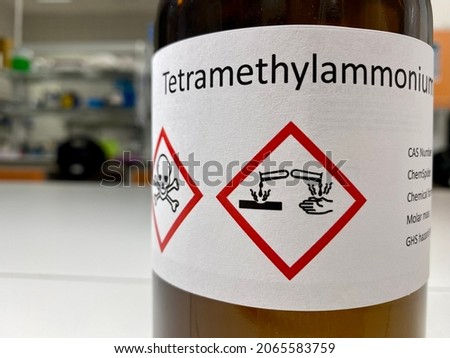 Dark glass bottle with an information label containing name of a chemical agent, safety symbols (corrosive, toxic), CAS number and other basic identifiers.