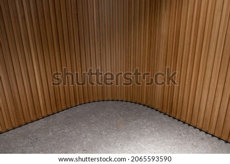Curving ribbed wood wall and stone floor combination. Wooden textured panel and gray stone tile. Interior design detail round corner.