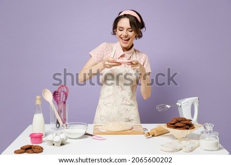 Young amazed housewife housekeeper chef baker woman in pink apron work at table kitchenware taking photo picture by mobile cell phone isolated on pastel violet background Process cooking food concept