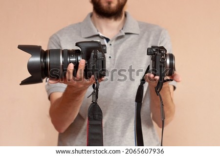 Man is holding in one hand dslr camera and mirrorless in another one. Comparison of two cameras for shooting. Choosing before buying and evaluating the pros and cons of cameras Royalty-Free Stock Photo #2065607936
