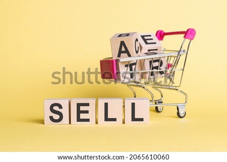 The word SELL on wooden cubes, on a yellow background with a shopping trolley.