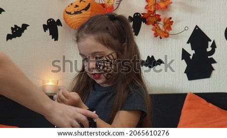 The girl makes funny faces, plays with a cloak for halloween. trick or treat. A girl in a devil costume, with horns on her head, a spider web make-up on her face. merry and happy halloween
