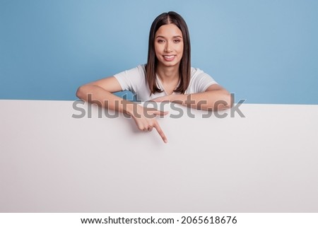 Portrait of cute promoter adviser lady direct finger down white wall billboard empty space on blue background