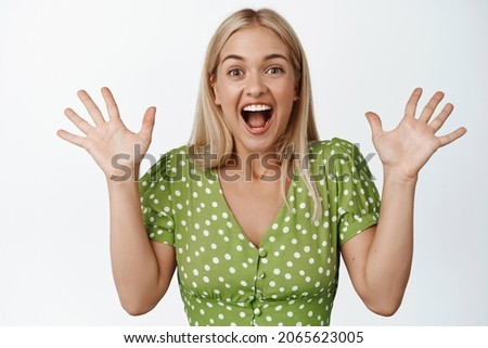 Happy and surprised blond girl cheering, celebrating, hear great announcement and rejoicing, standing over white background